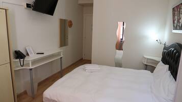 Ein Hotelzimmer mit einem Bett, einem Schreibtisch mit Telefon, einem flachbildfernseher an der Wand und einem Spiegel.