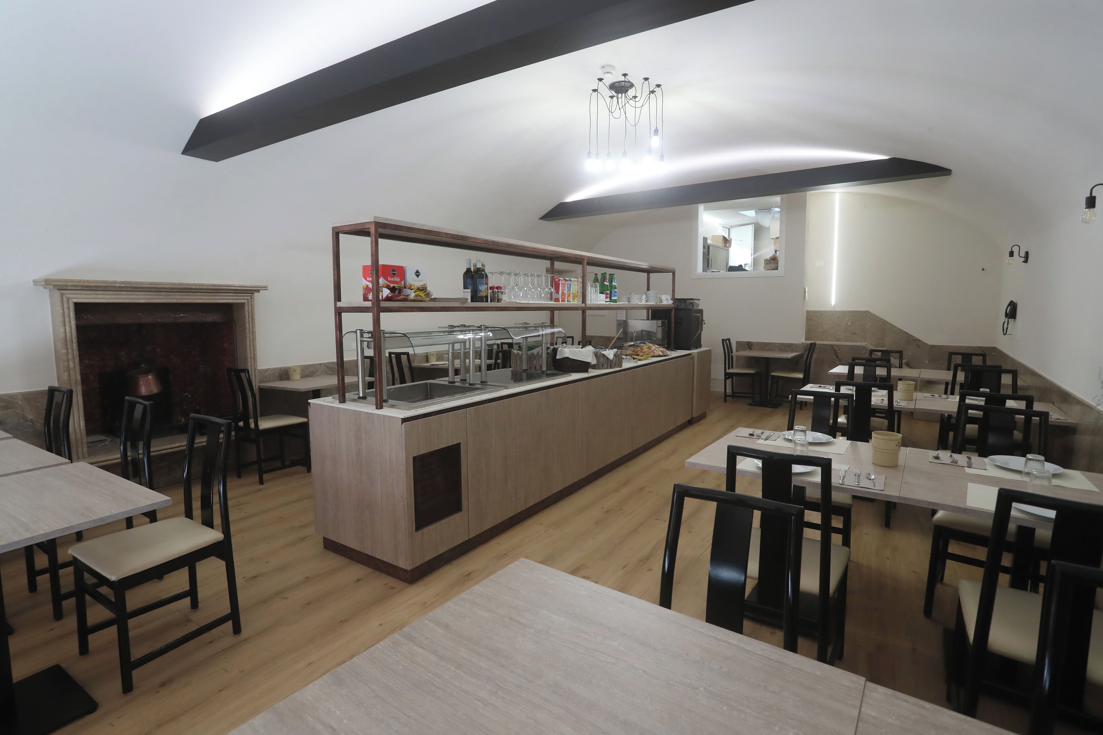 A modern restaurant with wooden tables and chairs, a central bar area, and a fireplace.