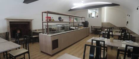 A modern restaurant with wooden tables and chairs, a central bar area, and a fireplace.