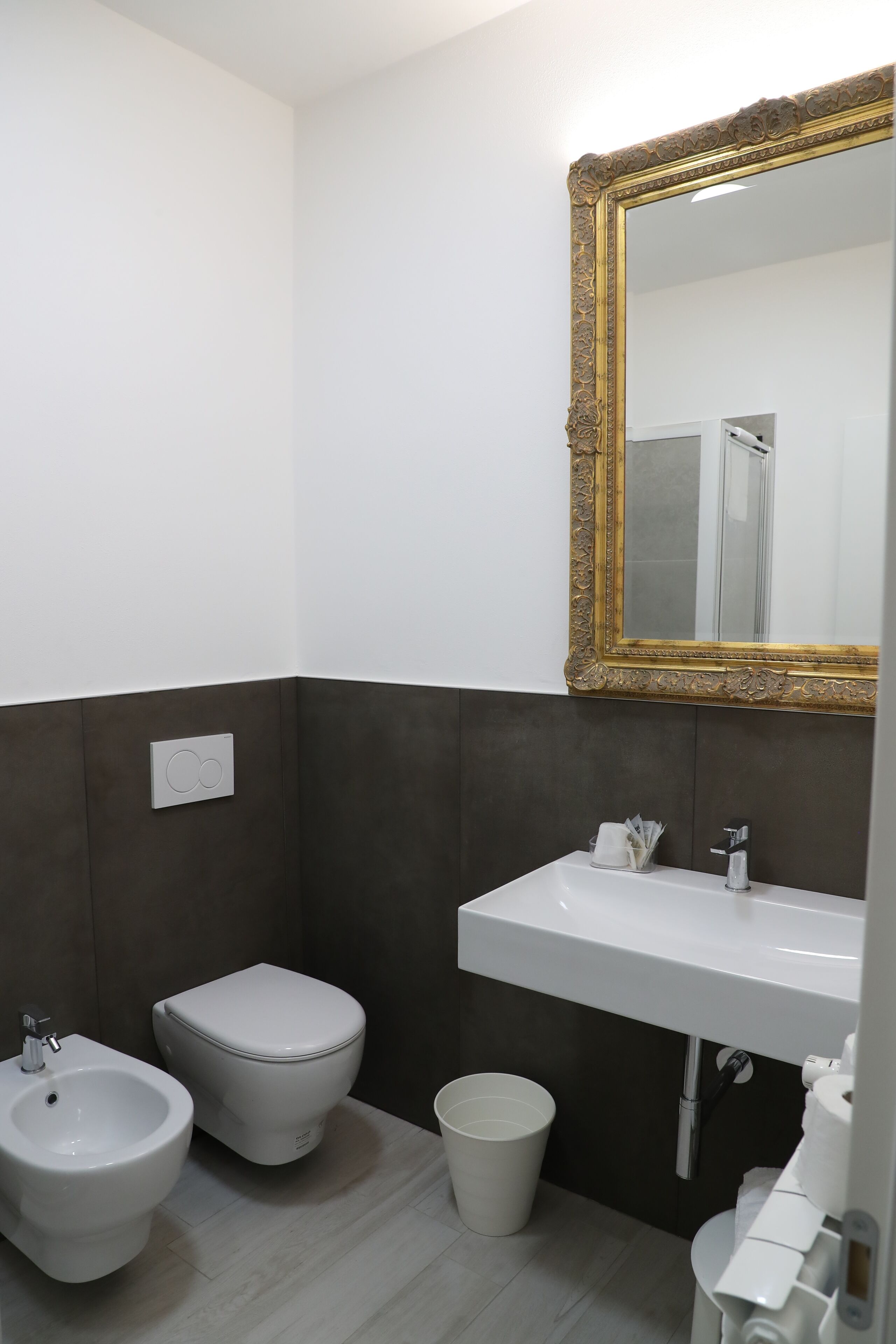 A bathroom with a white sink, a bidet, a toilet, and a large mirror with an ornate frame.