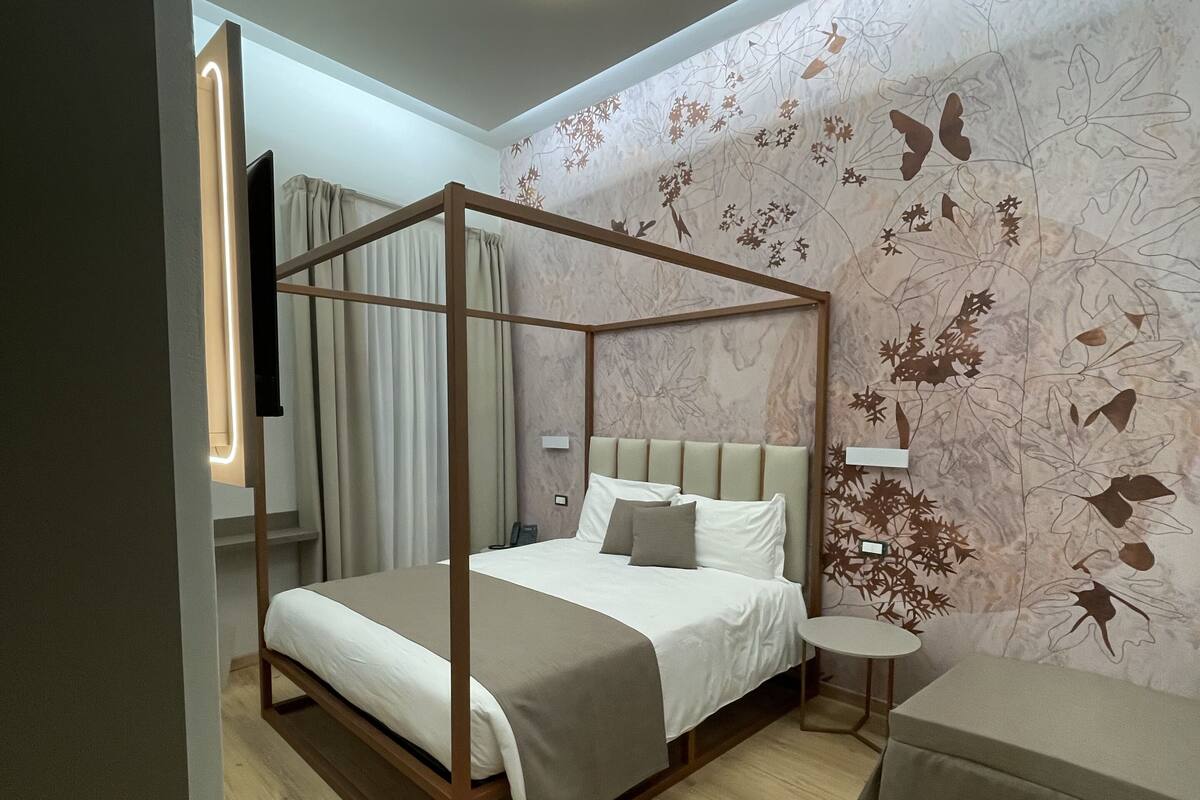 A modern bedroom with a four-poster bed, a small bedside table, and a wall-mounted TV.