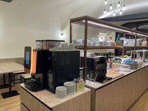 Eine Selbstbedienungs-Kaffeestation mit einer digitalen Kaffeemaschine, einer Glaskuppel und verschiedenen Kaffeetassen und Untertassen.
