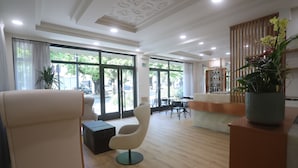 Un vestíbulo de hotel moderno con una recepción, zona de estar y amplios ventanales con vistas al exterior.