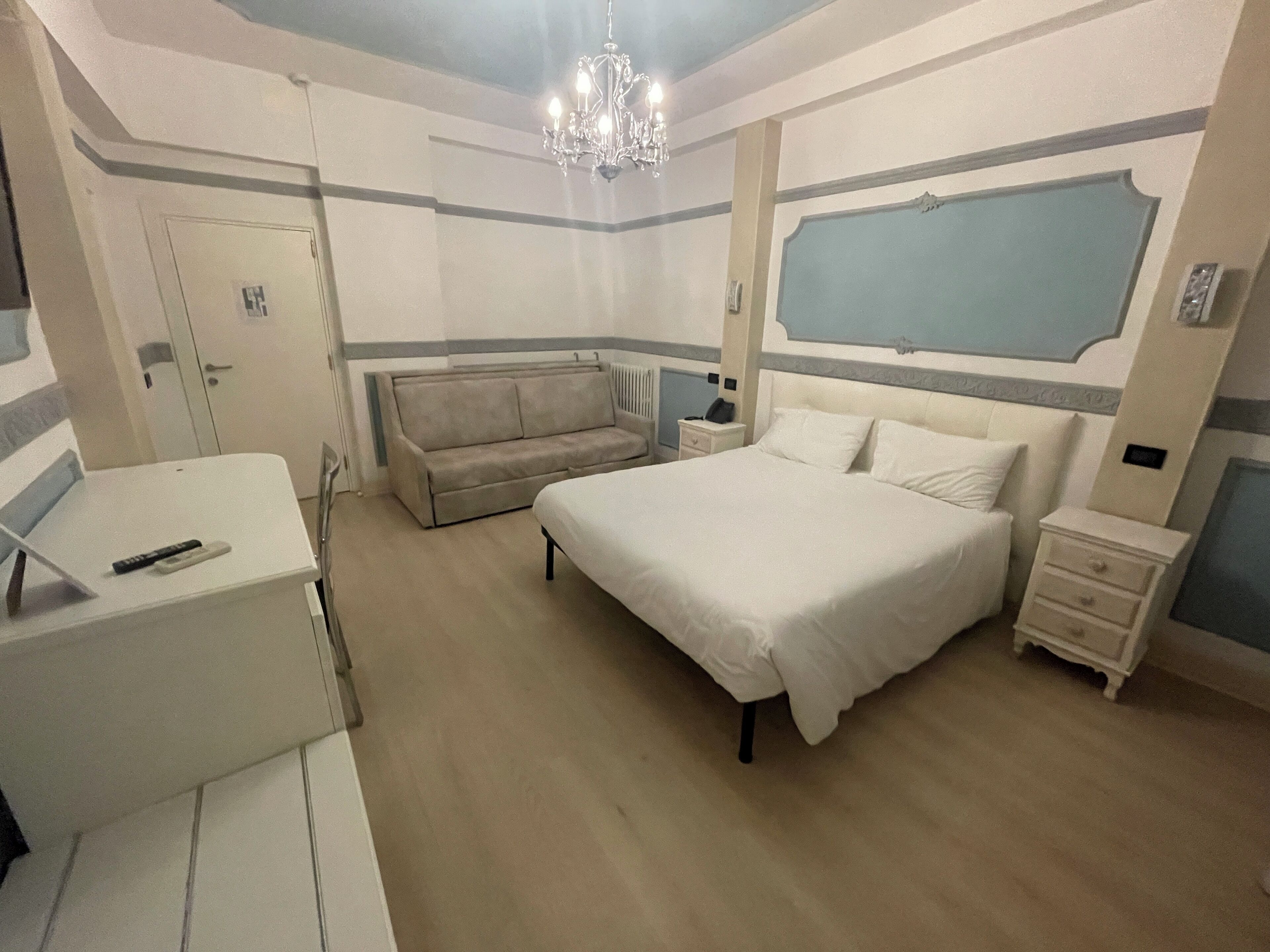 A bedroom with a bed, bedside tables, a sofa, a desk, and a chandelier.
