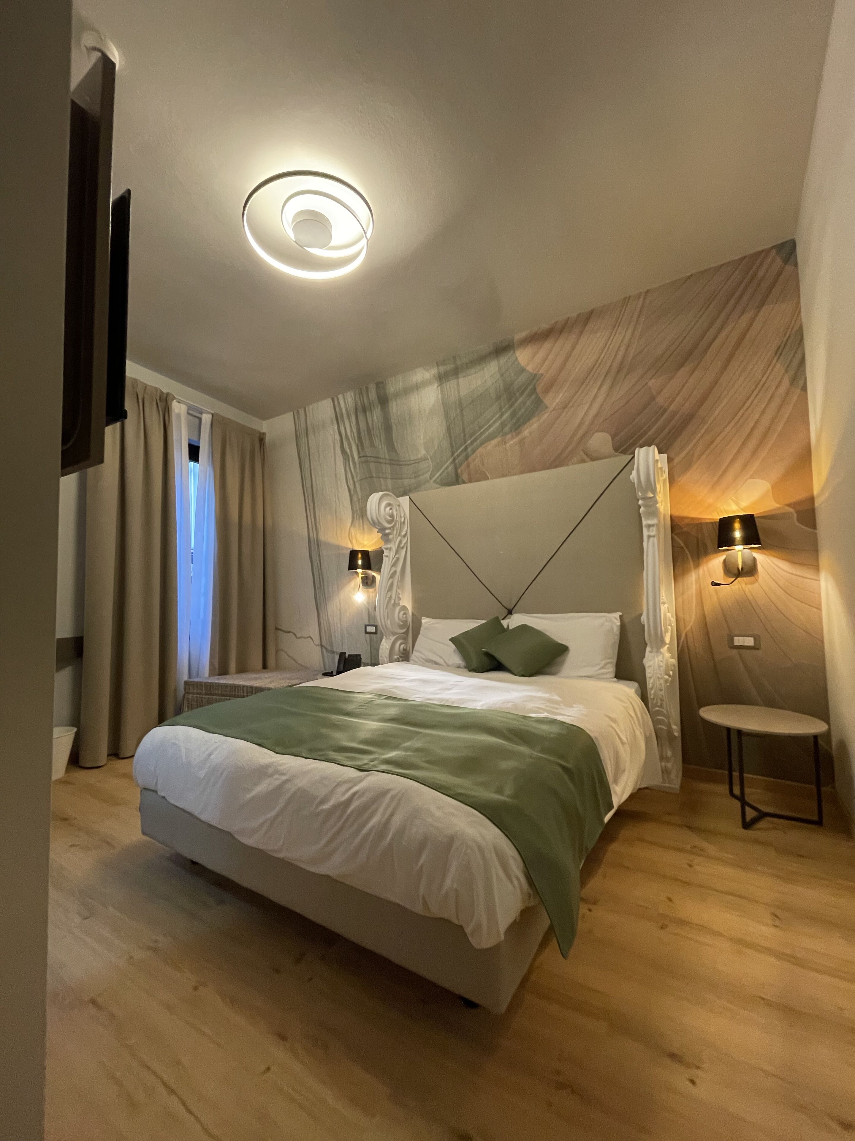 A modern bedroom with a large bed, two bedside lamps, a small table, and a unique ceiling light fixture.