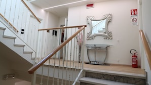 Una escalera con barandillas blancas y pasamanos de madera, un espejo en la pared y un extintor en el rellano.