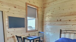Une pièce aux murs en bois, avec un lit, un bureau et deux chaises, une fenêtre et un tapis à motifs.