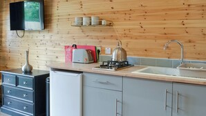 A kitchen with wooden walls, a gas stove, a kettle, a toaster, and a sink.
