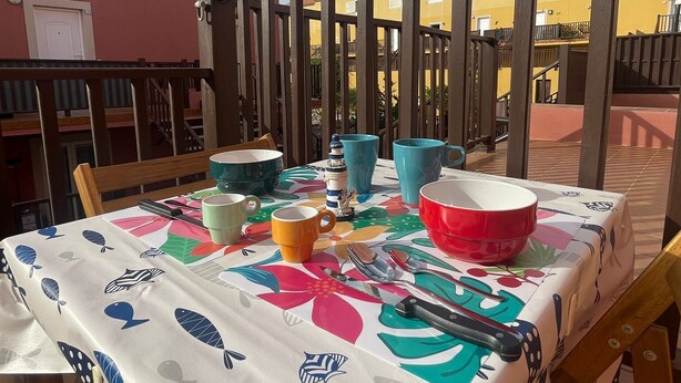 A table set outdoors with a colorful tablecloth, surrounded by a wooden fence, and buildings in the background.