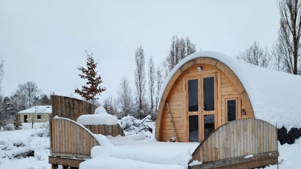 Une cabane en bois avec un toit arrondi, entourée d’un paysage enneigé et d’arbres.