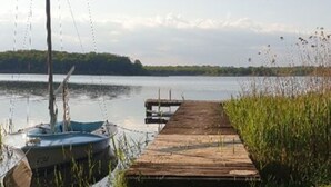 Une jetée en bois s’avance sur un lac paisible, et un voilier est amarré à son extrémité.