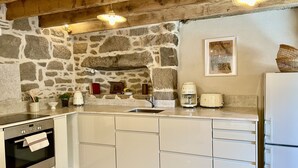 Eine Küche mit Steinwand, Holzbalken an der Decke, einem Bosch-Ofen, einer Spüle, einer Kaffeemaschine und einem Toaster.