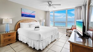 A hotel room with a bed, a ceiling fan, a TV, a window with a view of the ocean, and a painting on the wall. - Gulfside 1302 - Gulf Front! Community Pool! Hot Tub! Fitness Center! Tennis! (Miramar Beach)