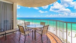 A balcony with a round table and four chairs, overlooking a beach with clear turquoise waters and a sandy shore. - Gulfside 1302 - Gulf Front! Community Pool! Hot Tub! Fitness Center! Tennis! (Miramar Beach)