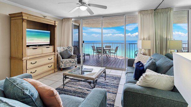 A spacious living room with a television, a ceiling fan, a balcony with a table and chairs, and a view of the ocean. - Gulfside 1302 - Gulf Front! Community Pool! Hot Tub! Fitness Center! Tennis! (Miramar Beach)