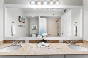 A bathroom with a large mirror, two sinks, a shower, and a toilet.