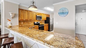 A kitchen with granite countertops, wooden cabinets, stainless steel appliances, and a wall clock. - Gulfside 1302 - Gulf Front! Community Pool! Hot Tub! Fitness Center! Tennis! (Miramar Beach)