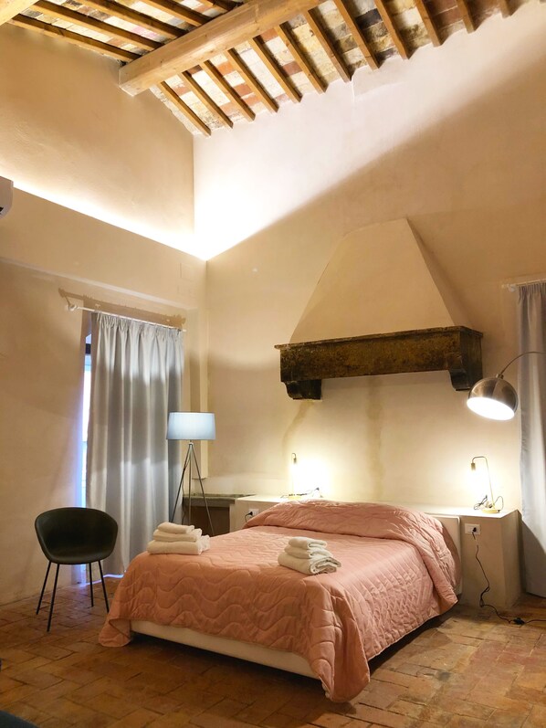 A bedroom with a sloped ceiling, a bed with pink bedding, a desk with a lamp, and a chair.