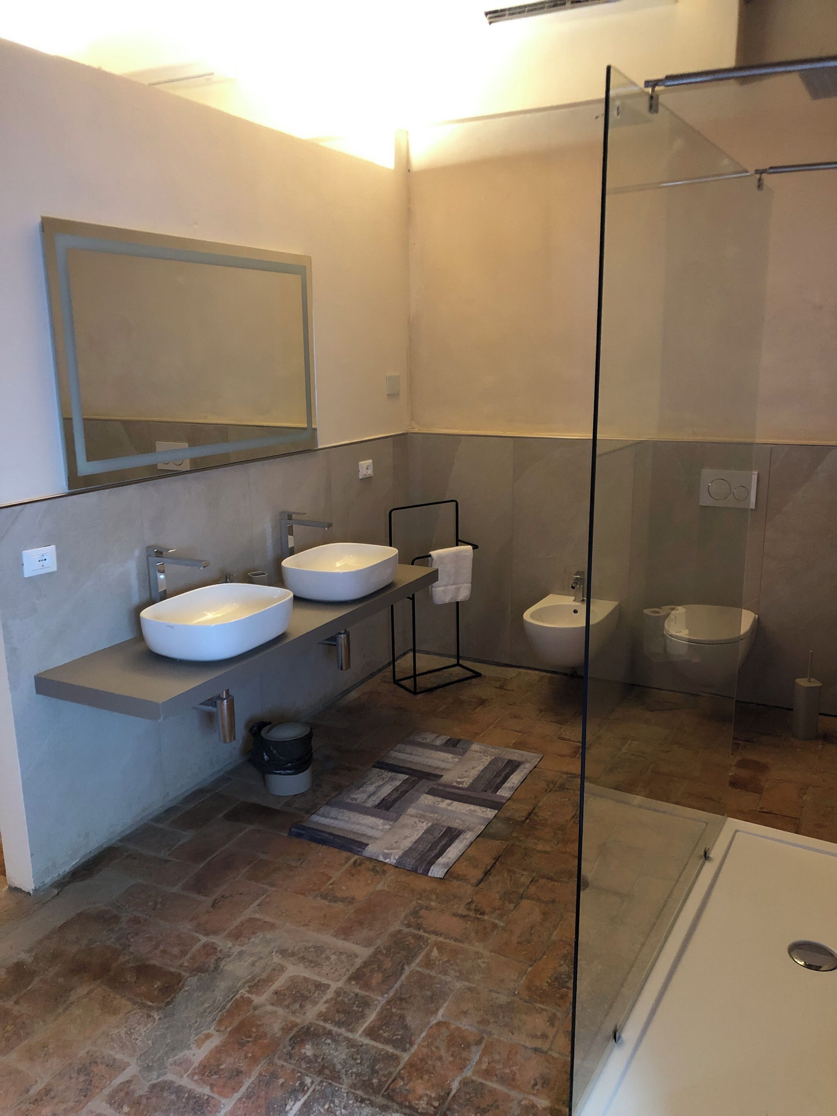 Une salle de bain moderne dotée d’une douche à parois de verre, de deux lavabos, de toilettes et d’un bidet.