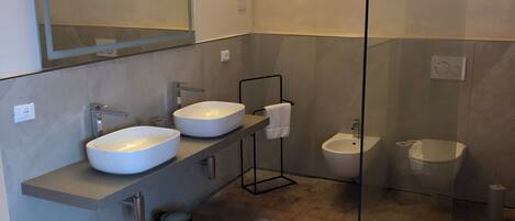 Une salle de bain moderne dotée d’une douche à parois de verre, de deux lavabos, de toilettes et d’un bidet.