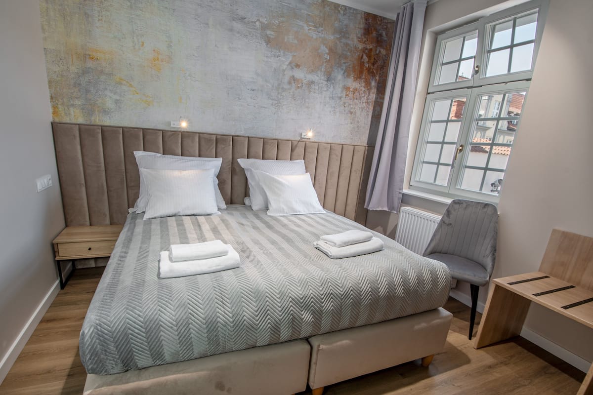 Een net opgemaakt bed met een gestreept dekbedovertrek, twee kussens en opgevouwen handdoeken.
