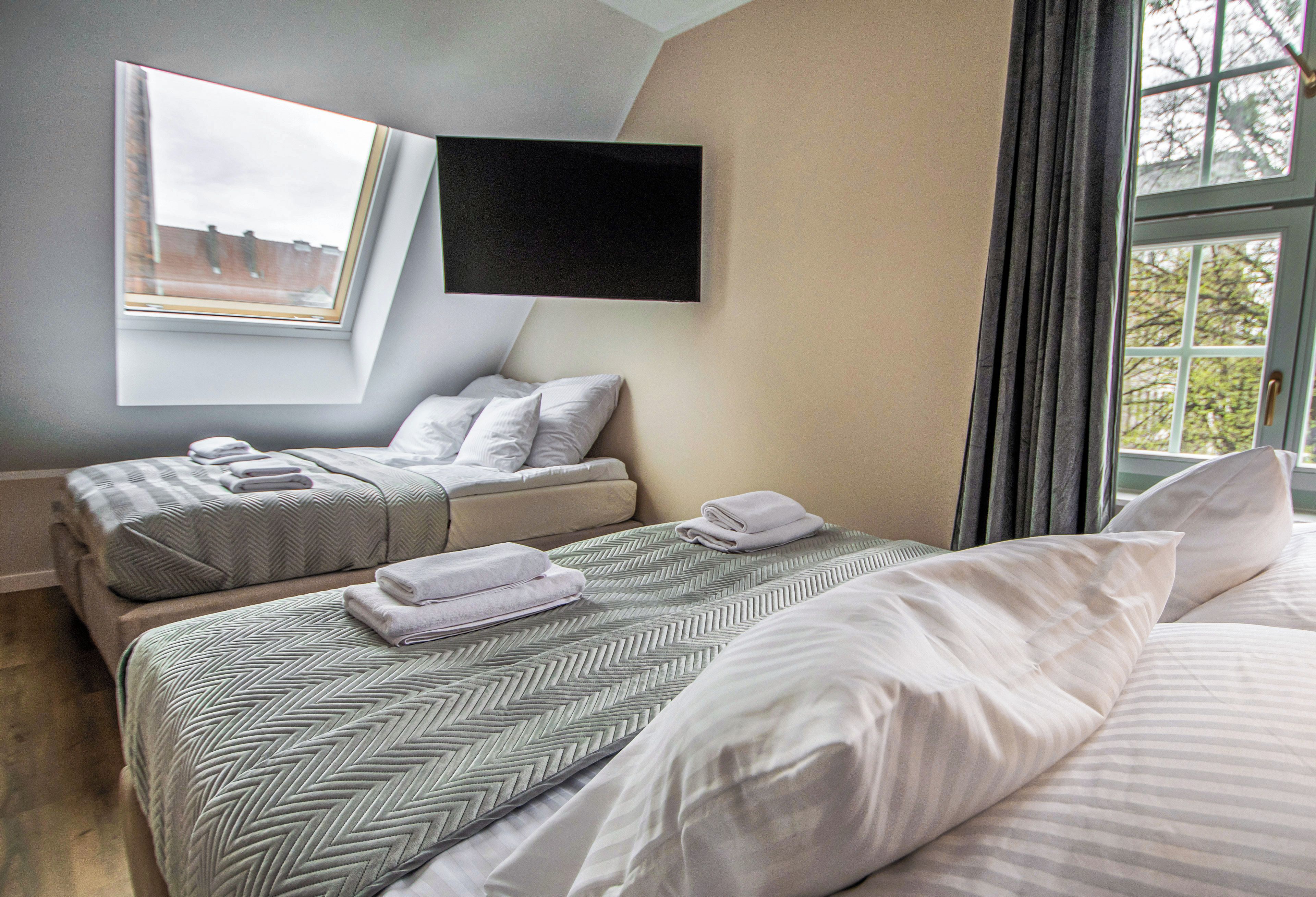 A hotel room with two beds, a flat-screen TV mounted on the wall, and a window with curtains.