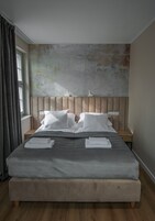 A bedroom with a large bed, a headboard, a bedside table, and a window with curtains.