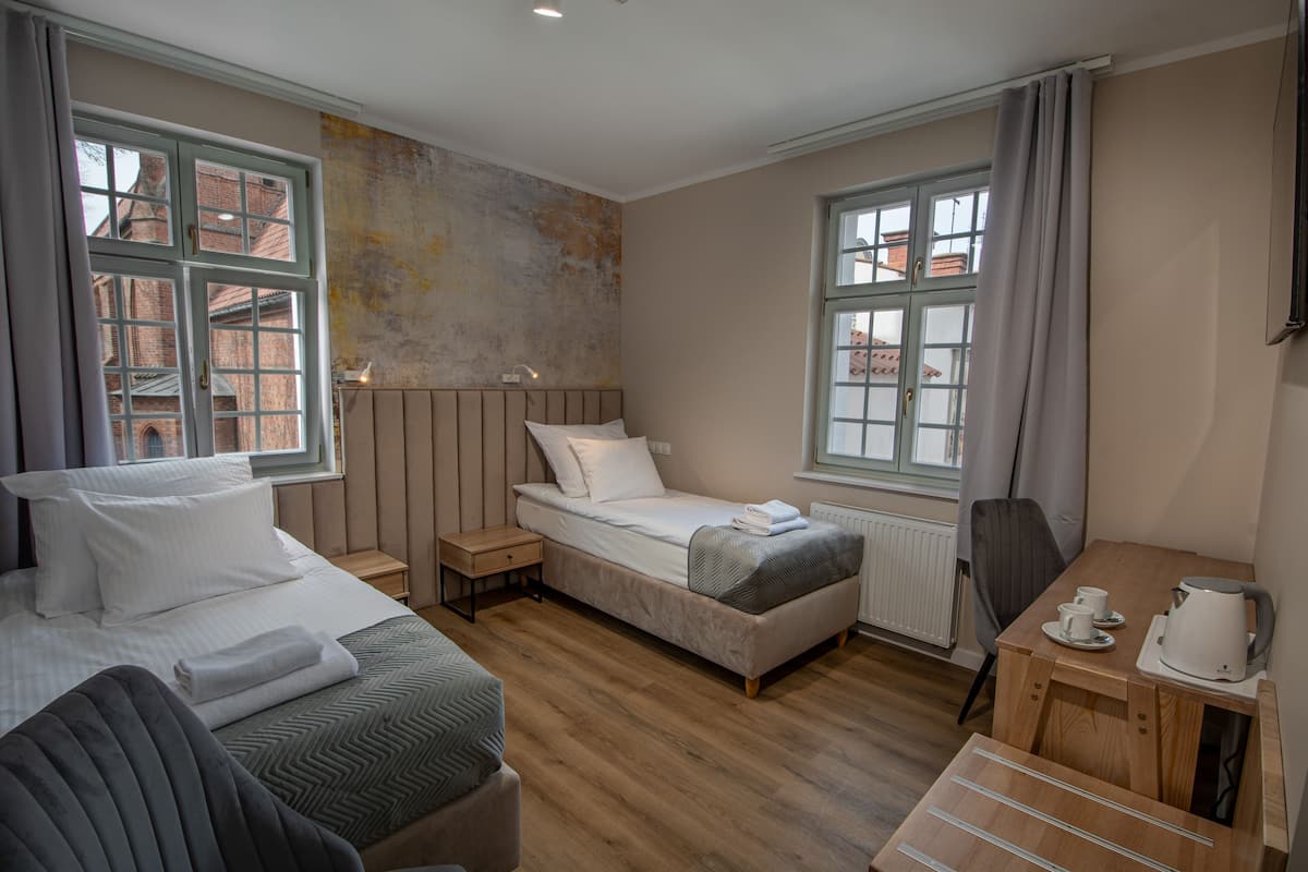 Een compacte slaapkamer met een bed, nachtkastje en een klein houten bureau met een waterkoker.