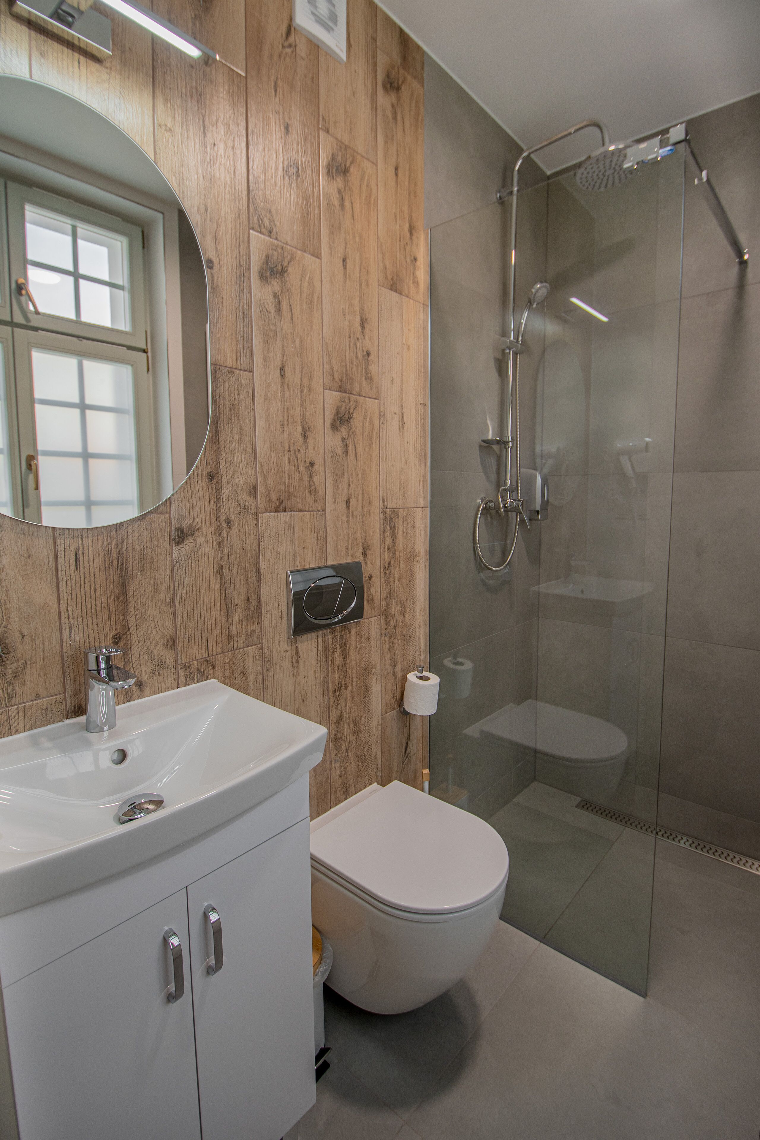 Ein Badezimmer mit Holzwand, Waschbecken in Weiß, Toilette und einer Duschkabine aus Glas.