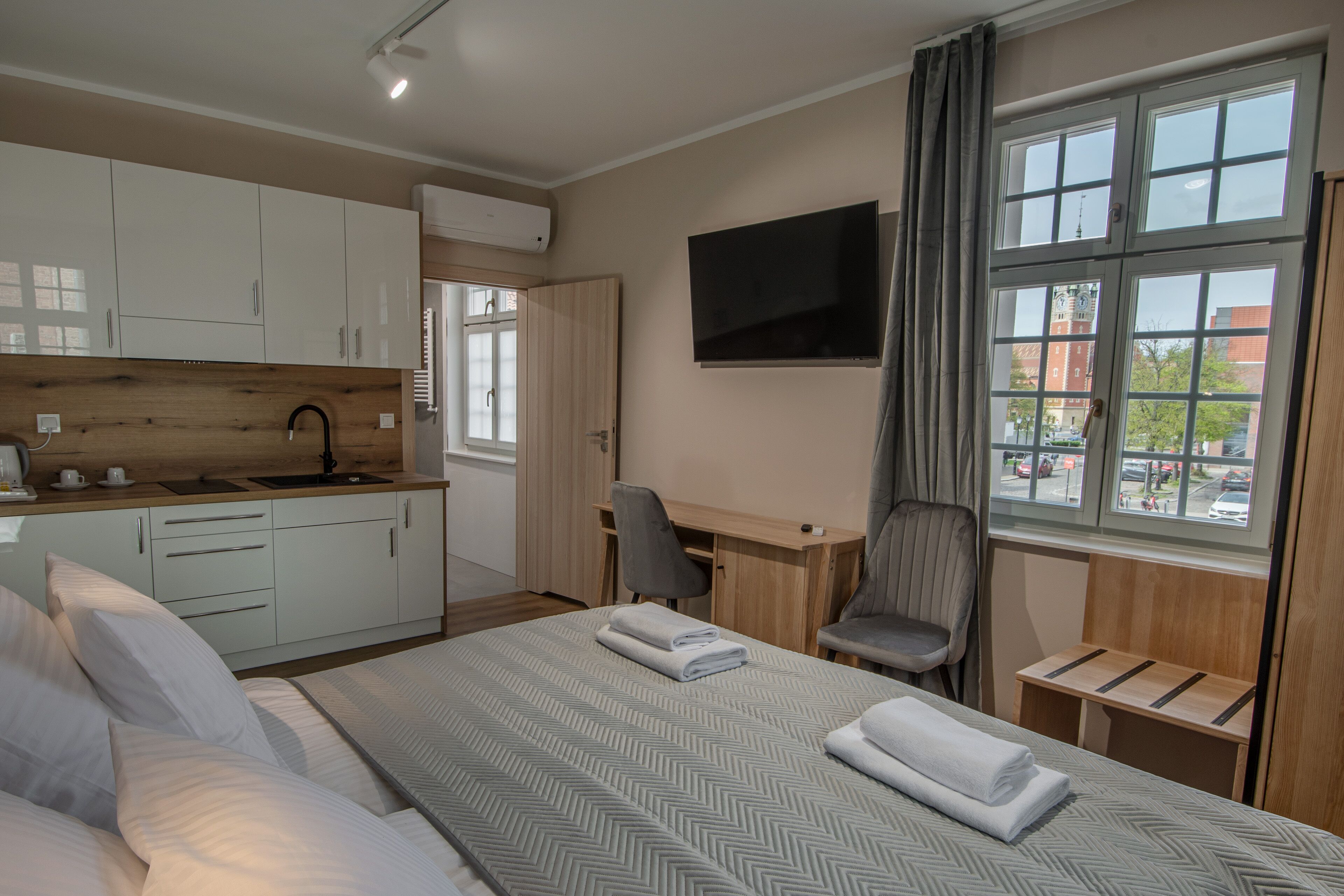 A hotel room with a bed, a desk, a chair, a TV, and a window with a view of buildings.