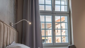 Une chambre d’hôtel avec un lit, une chaise, une fenêtre avec des rideaux et un luminaire fixé au mur.