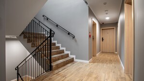 Un escalier avec des marches en bois et des rampes noires, menant à un couloir doté d’un plancher en bois et d’une porte au fond.