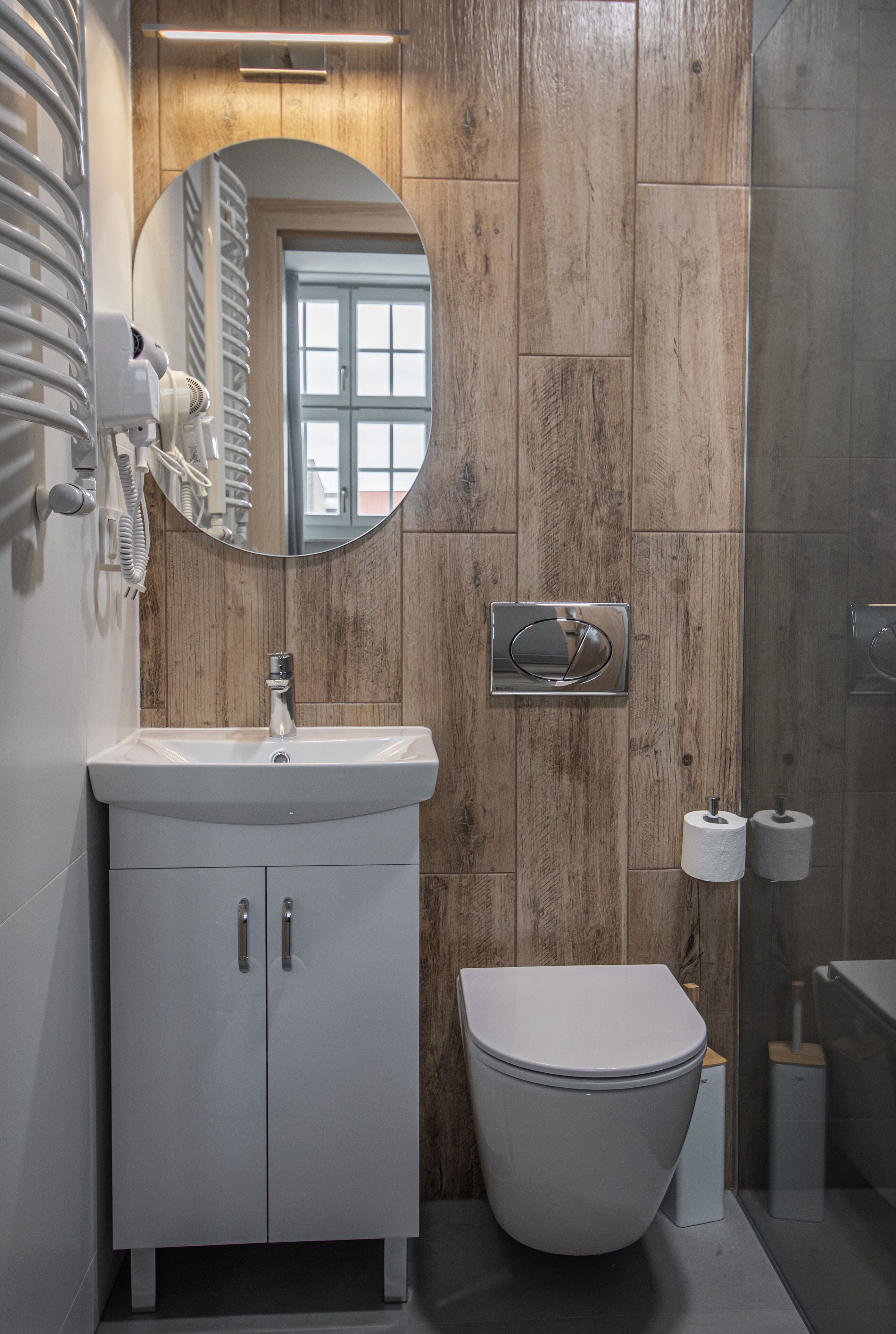 A modern bathroom with a wooden wall, a white sink, a toilet, and a mirror.