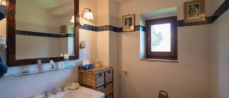 A bathroom with a white sink, a mirror, and a toilet. There are two framed pictures on the wall, and a window above the toilet.