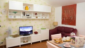 A living room with a TV, white cabinets, a red sofa, and a dining table with pastries.