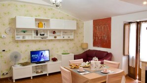 A living room with a TV, white shelves, a red sofa, and a dining table set.