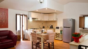 A compact kitchen with white cabinets, a dining table with chairs, a refrigerator, and a microwave.