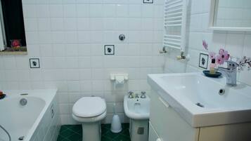 Et badeværelse med hvide fliser, grøn gulv, et badekar, et toilet, en bidet og en vask med et spejl.