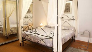 A four-poster bed with a canopy, a small bedside table with a lamp, and a framed picture on the wall.