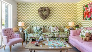 Una sala de estar con sofás de estampado floral, una mesa de centro con juegos de mesa y una decoración de pared con forma de corazón.