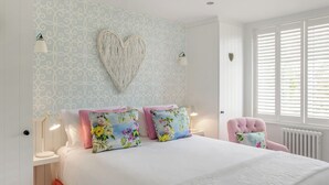 Un dormitorio con cama, dos lámparas de noche, un adorno en forma de corazón y una ventana con persianas.