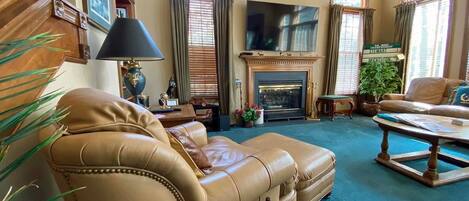 Una sala de estar con chimenea, muebles de cuero, un televisor y una estantería.