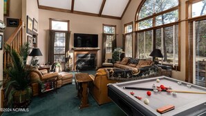 Un salon spacieux avec une table de billard, des sièges confortables, une cheminée et de grandes fenêtres.
