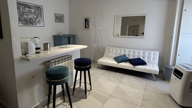 Ein kompakter Wohnraum mit Küchenzeile, einem weißen Sofa mit blauen Kissen und einer kleinen Bar mit Hockstühlen.