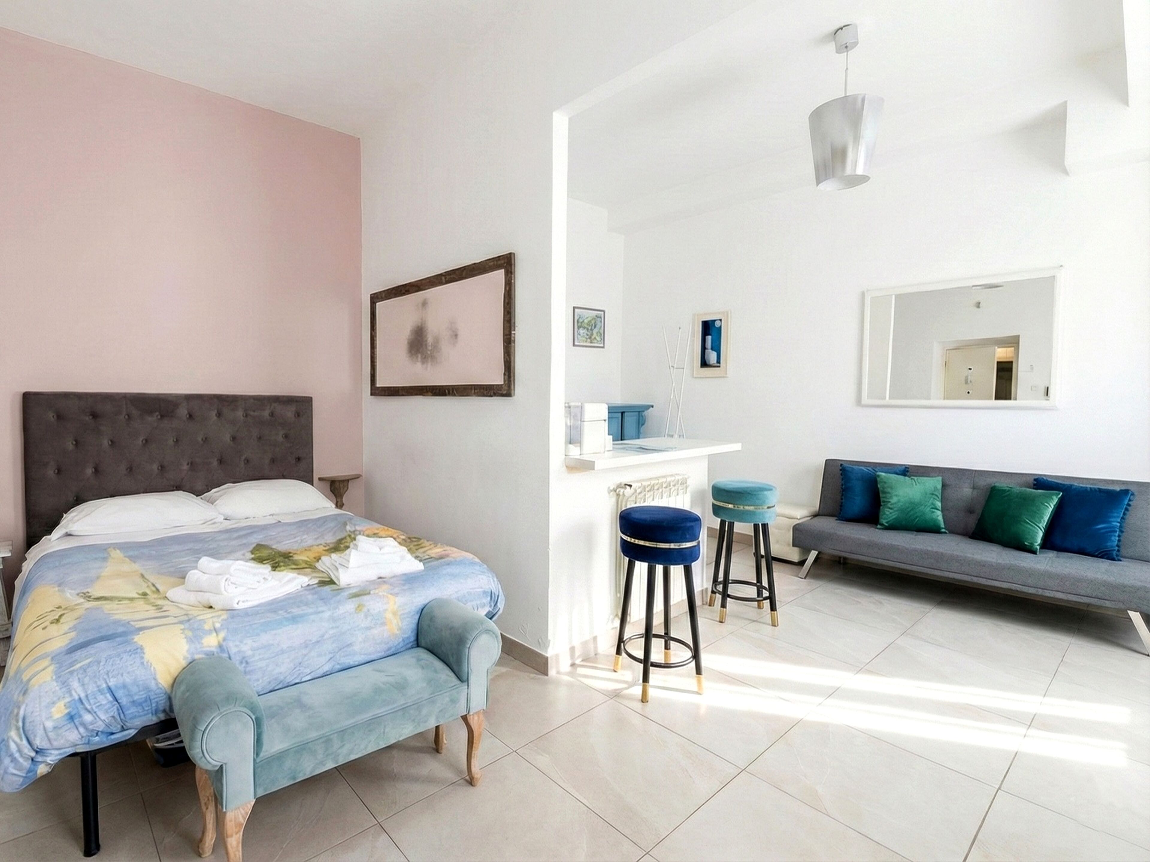 A bedroom with a bed, a sofa, a small bar area, and a mirror on the wall.