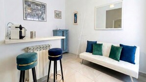 Un salon moderne avec un canapé blanc, deux tabourets de bar bleus, une table basse blanche et un meuble bleu.