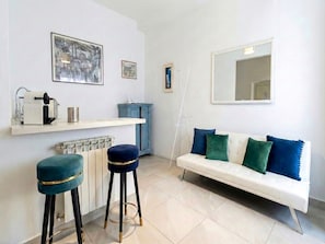 Un salon moderne avec un canapé blanc, deux tabourets de bar bleus, une table basse blanche et un meuble bleu.