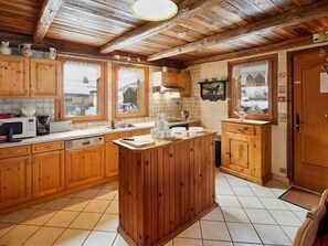 A kitchen with wooden cabinets, a central island, and a view of the outside through windows. - Chalet, wifi, sauna, fireplace or stove, parking, tv, 122m², Les Gets (Les Gets)
