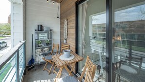 Eine Holzterrasse mit Tisch und Stühlen, ein kleines Regal mit Dekoration und Blick ins Freie.