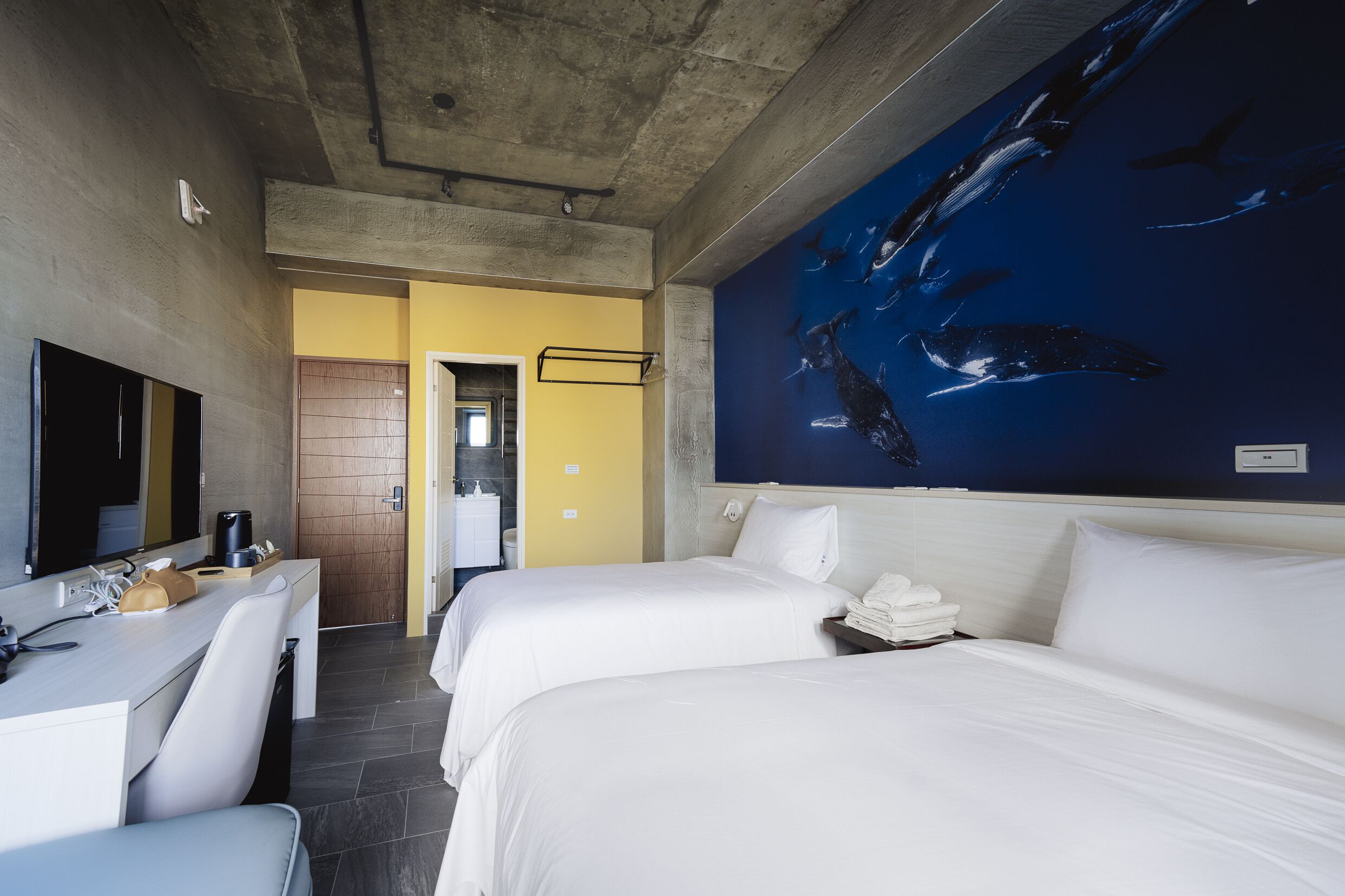 A hotel room with two beds, a desk, a mirror, and a wall mural of whales.